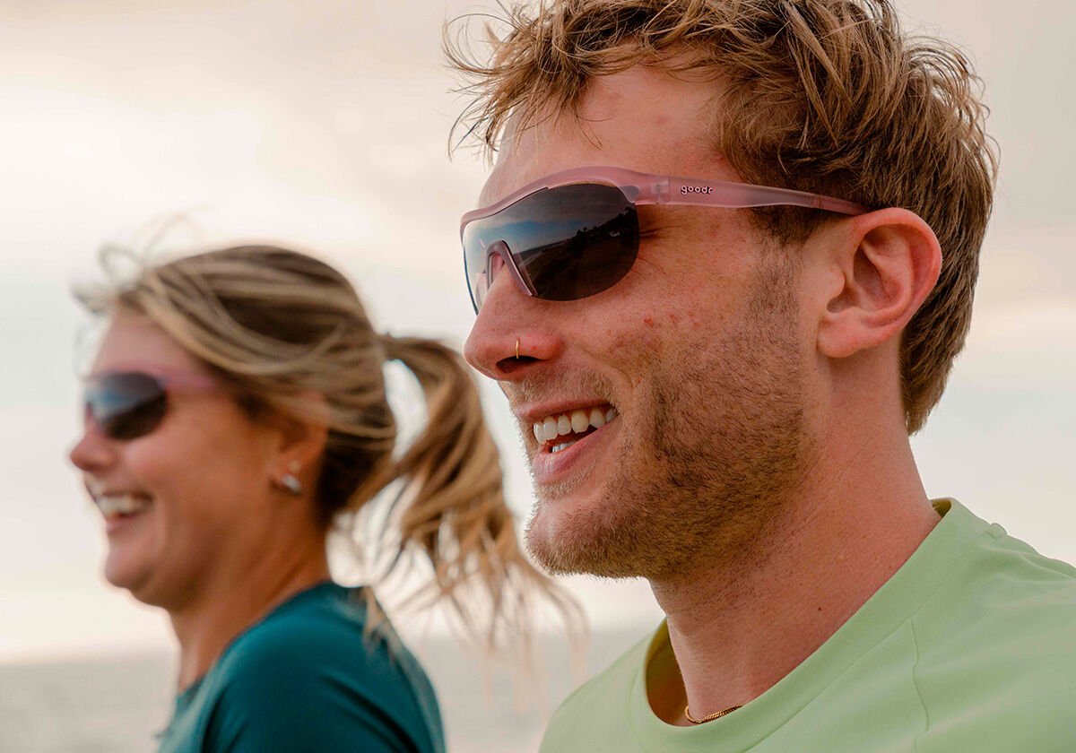 Casal sorrindo na praia usando óculos de sol